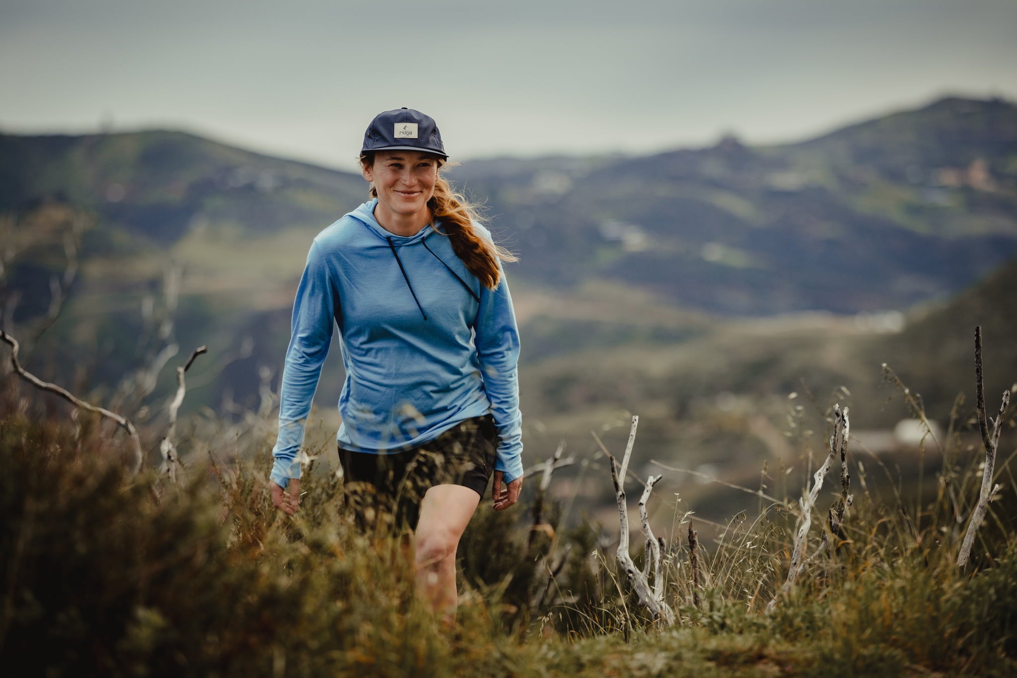 a woman hikes on a trail wearing the Solstice Merino Wool Sun Hoodie