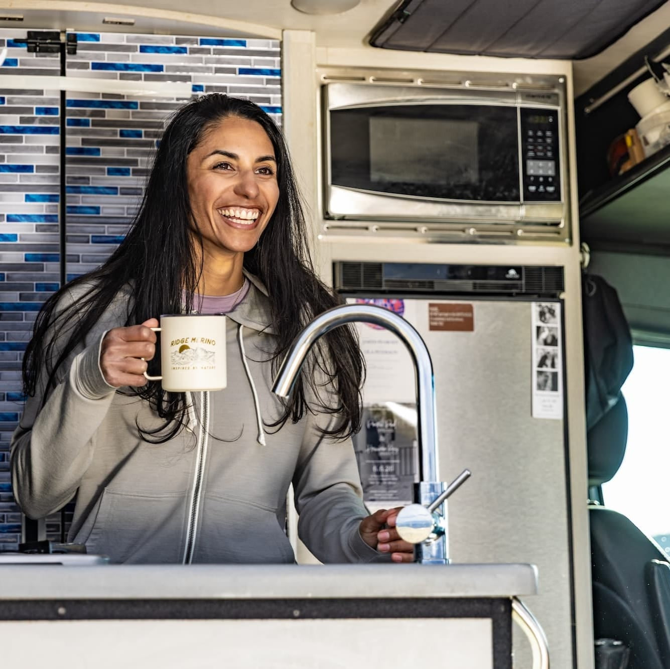 a woman drinks coffee in her van wearing a Ridge Merino Traveler Hoodie