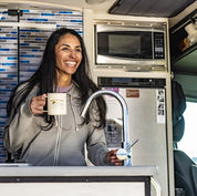 a woman drinks coffee in her van wearing a Ridge Merino Traveler Hoodie