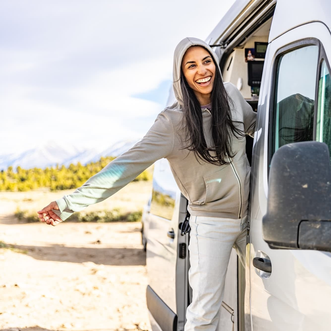a woman laughs leaning out the door of her camper van wearing a gray Traveler Hoodie