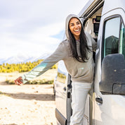 a woman laughs leaning out the door of her camper van wearing a gray Traveler Hoodie