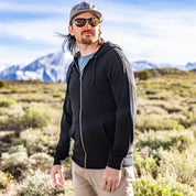 a man wearing a black Traveler Hoodie over a blue t-shirt in the mountains