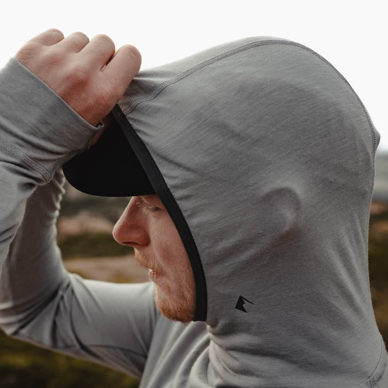 A man adjusts the Pursuit ultralight hoodie hood over his hat