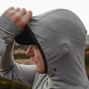 A man adjusts the Pursuit ultralight hoodie hood over his hat