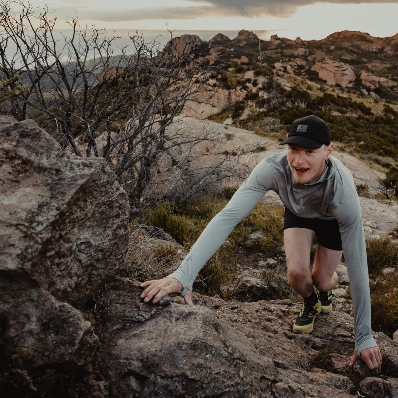 A man scrambles over rocks wearing the Pursuit hoodie and Ridge Run Hat