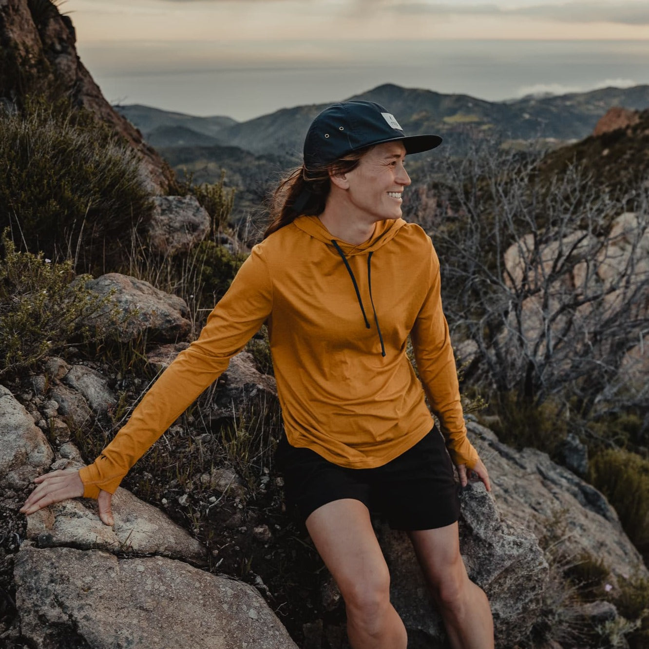 a woman wearing a Goldenrod Solstice Sun Hoodie and Ridge Merino hat on a trail run