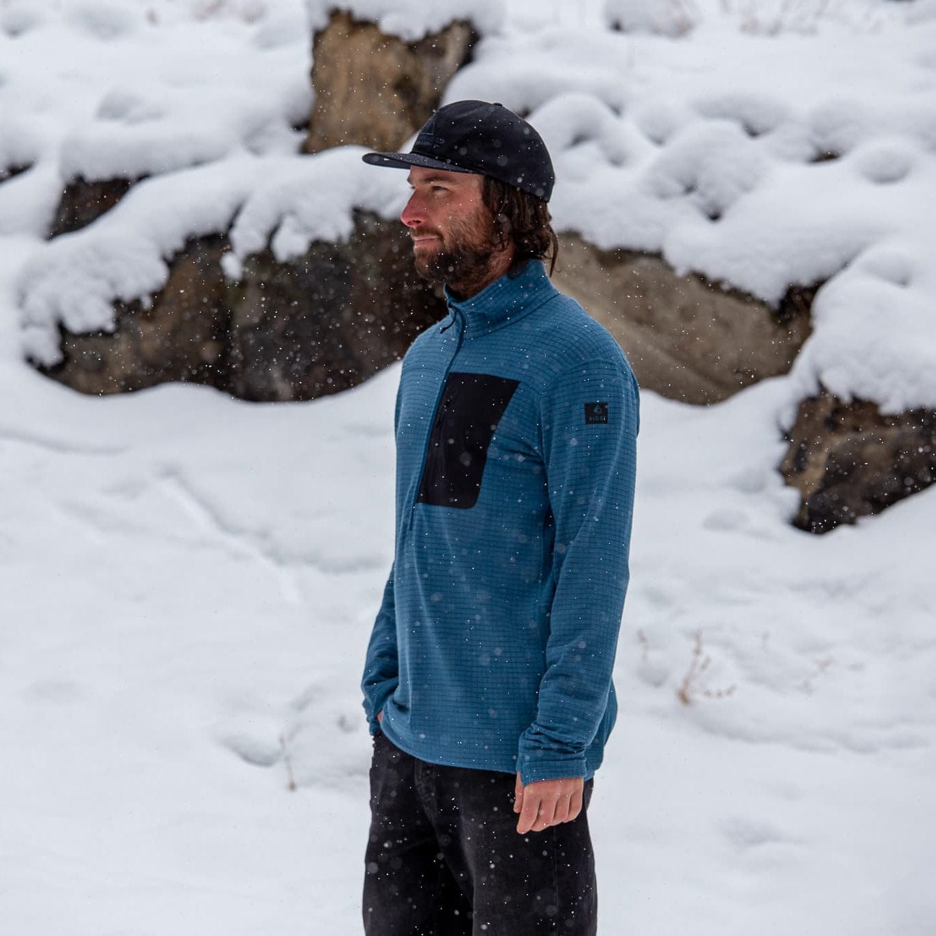 Person wearing a blue Cloudripper Grid Fleece Half Zip Pullover with a black pocket outside in the snow