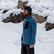 Person wearing a blue Cloudripper Grid Fleece Half Zip Pullover with a black pocket outside in the snow