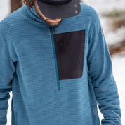 Person wearing a blue Cloudripper Grid Fleece Half Zip Pullover with a black pocket outside in the snow