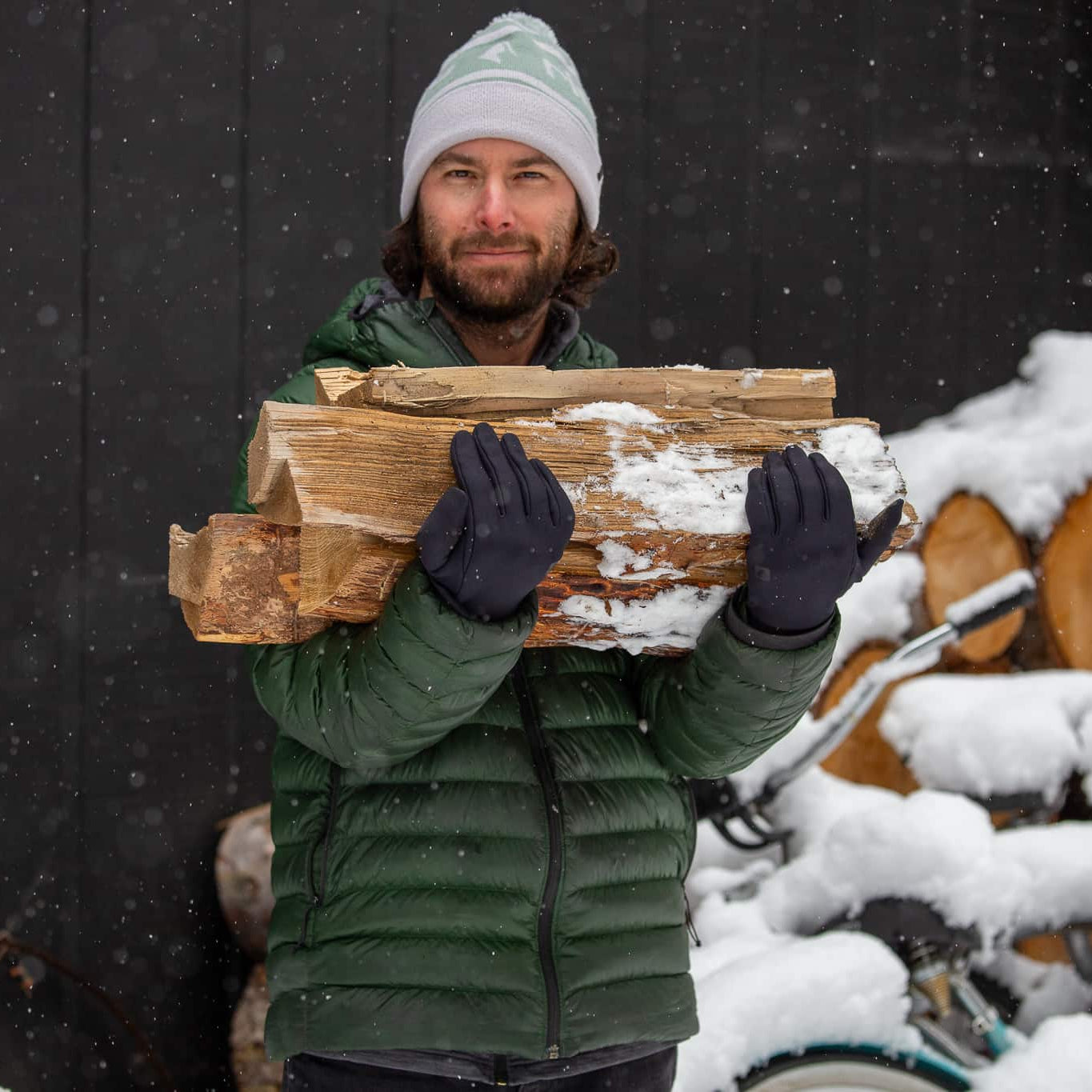 a man wearing a Ridge Team Beanie carrying firewood in the snow
