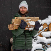 a man wearing a Ridge Team Beanie carrying firewood in the snow