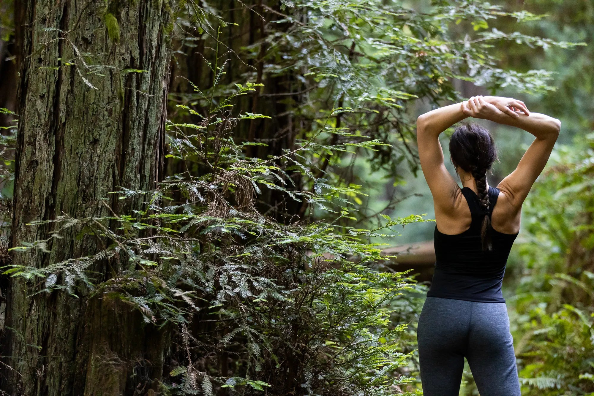 a woman stretches during a trail run wearing the Ridge Merino Wool Racerback Tank and joggers
