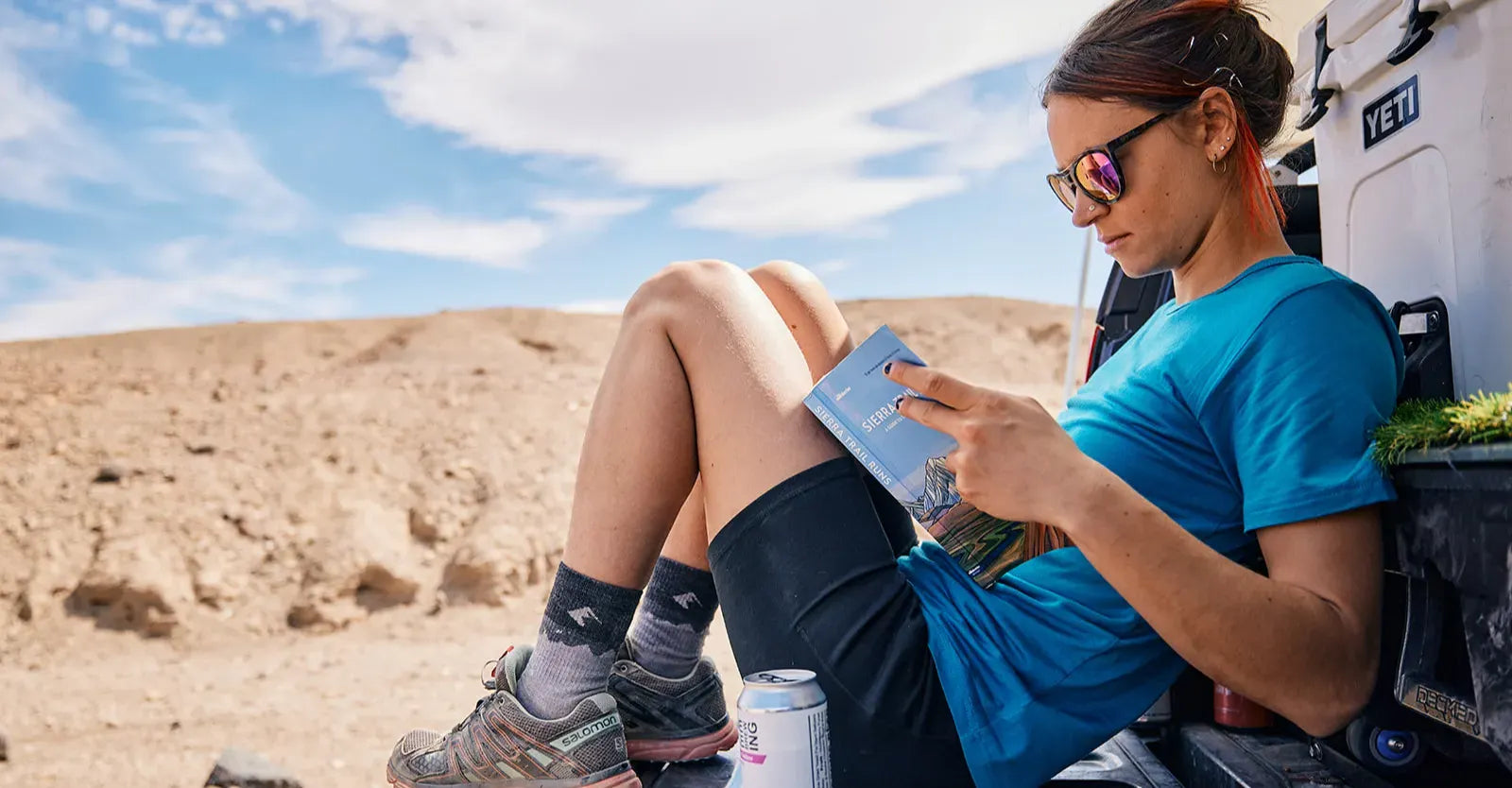 A woman reads the Sierra Trail Runs guide book in the back of a truck on a sunny warm day in the desert