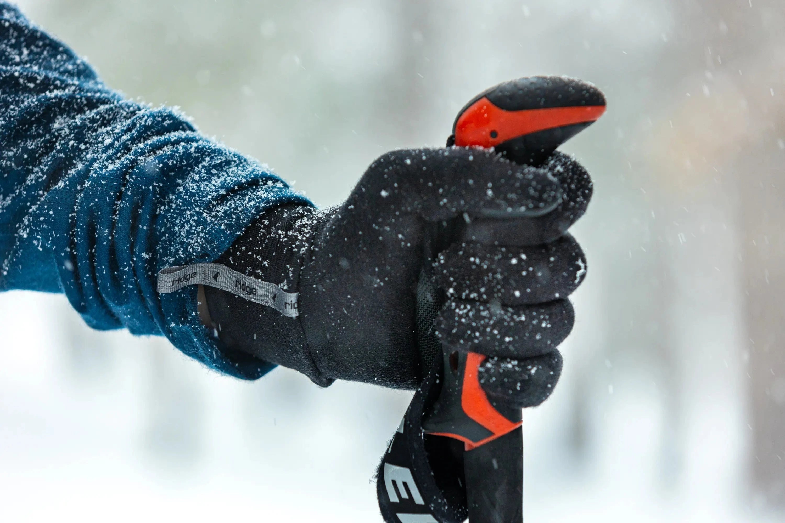 a close-up of a hand wearing a Ridge Liner Glove holding a ski pole on a snowy day