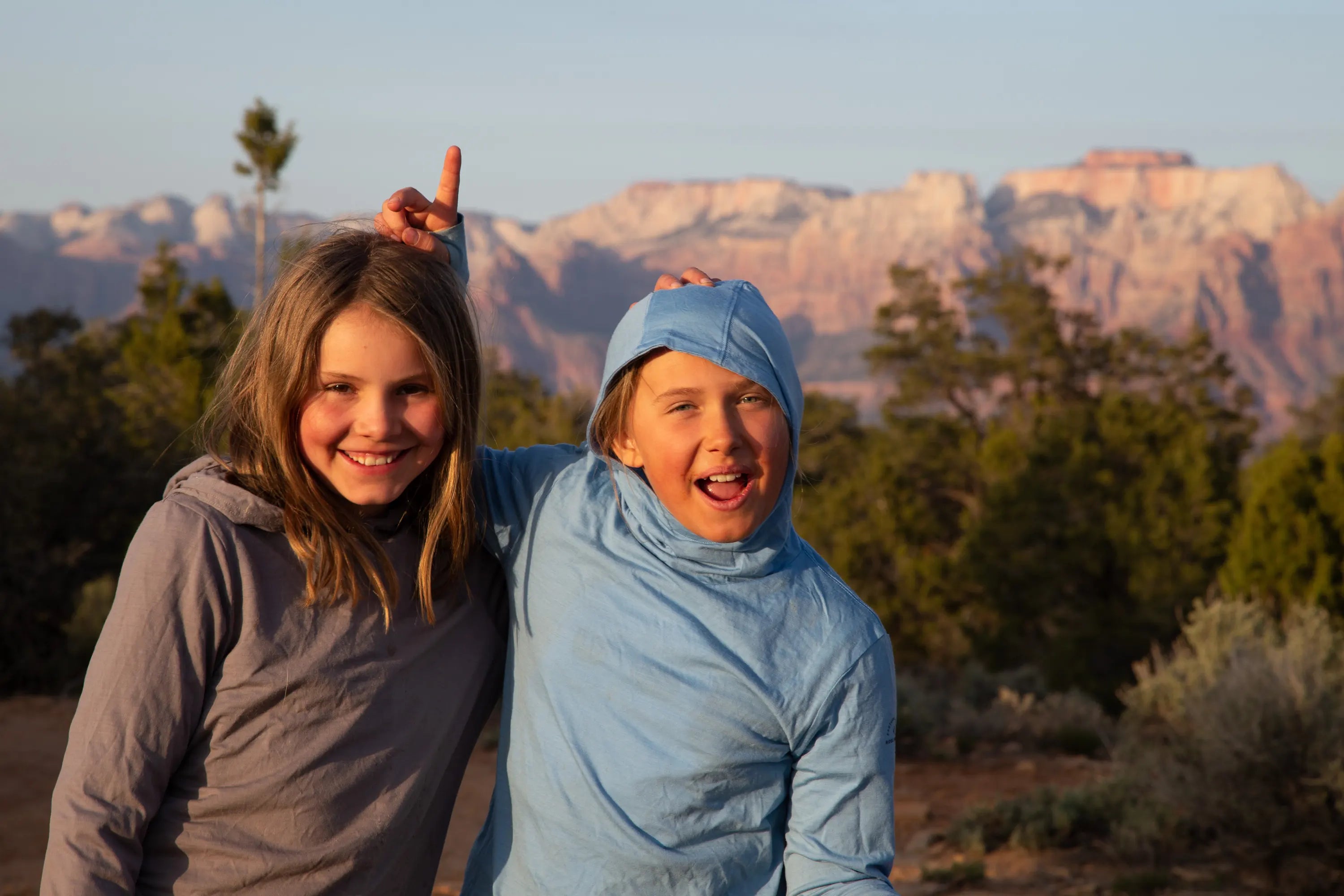 two kids smile wearing Ridge Merino Solstice sun hoodies in the desert