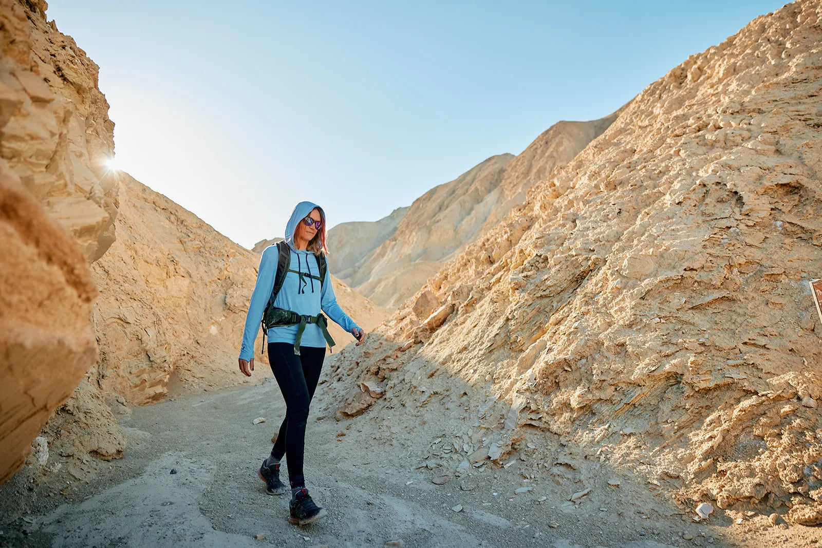 a woman walks through a canyon in Death Valley wearing a Ridge Merino Solstice sun hoodie