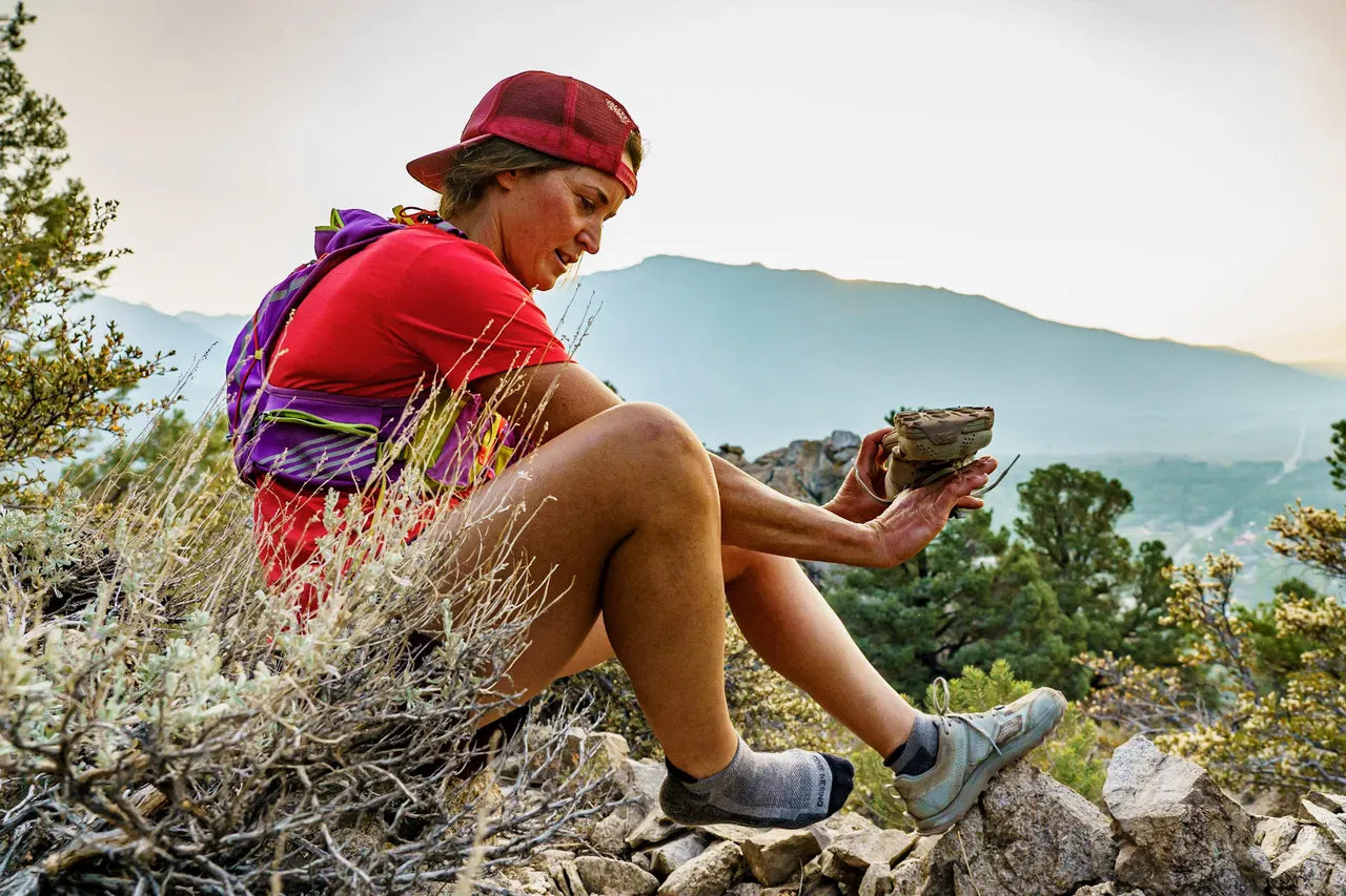 a woman takes a break on a trail run to empty pebbles from her shoes