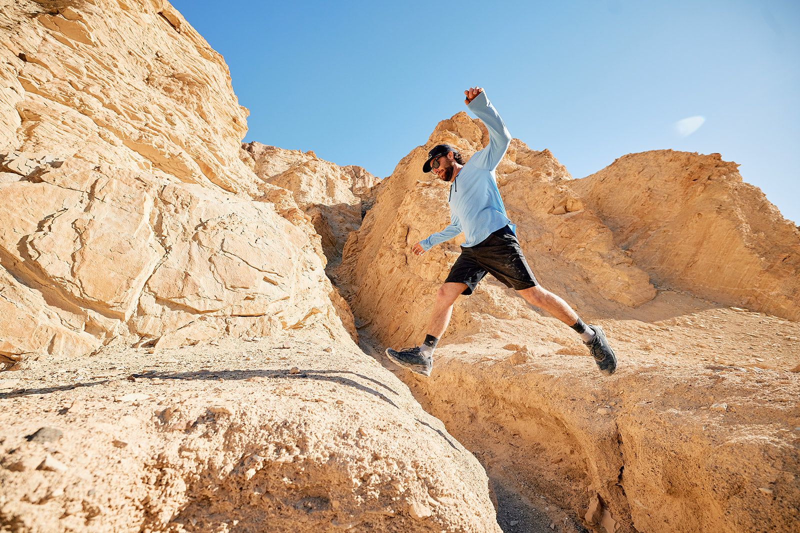 a man jumps from one rock to another in a desert playground wearing a Ridge Merino solstice hoodie