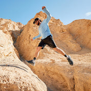a man jumps between two rocks wearing a blue Solstice Hoodie