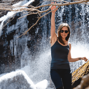 A woman smiles on a hike wearing sunglasses and the Ridge Merino wool shelf bra camisole